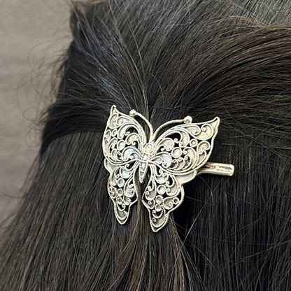 Silver butterfly hair clip on black hair against a neutral background