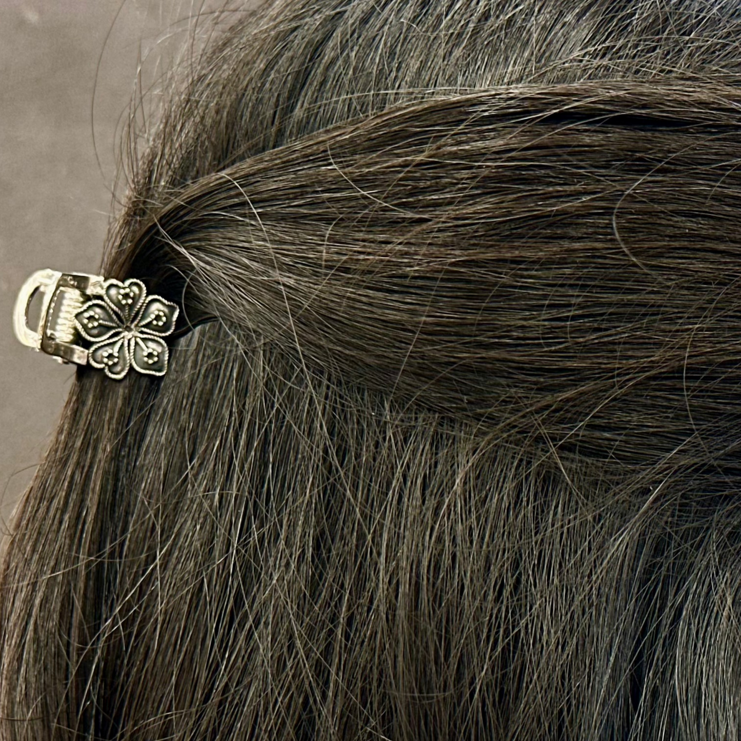 Close-up of a person's hair with a decorative hair clip against a neutral background
