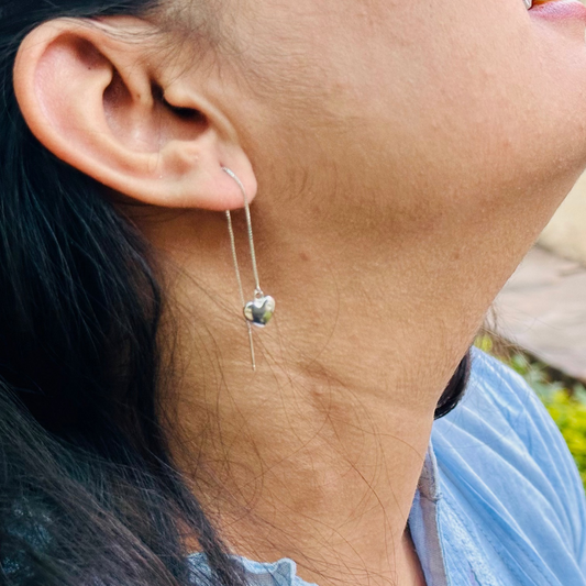 A close-up image of a woman's ear wearing a silver threader earring with a heart charm.