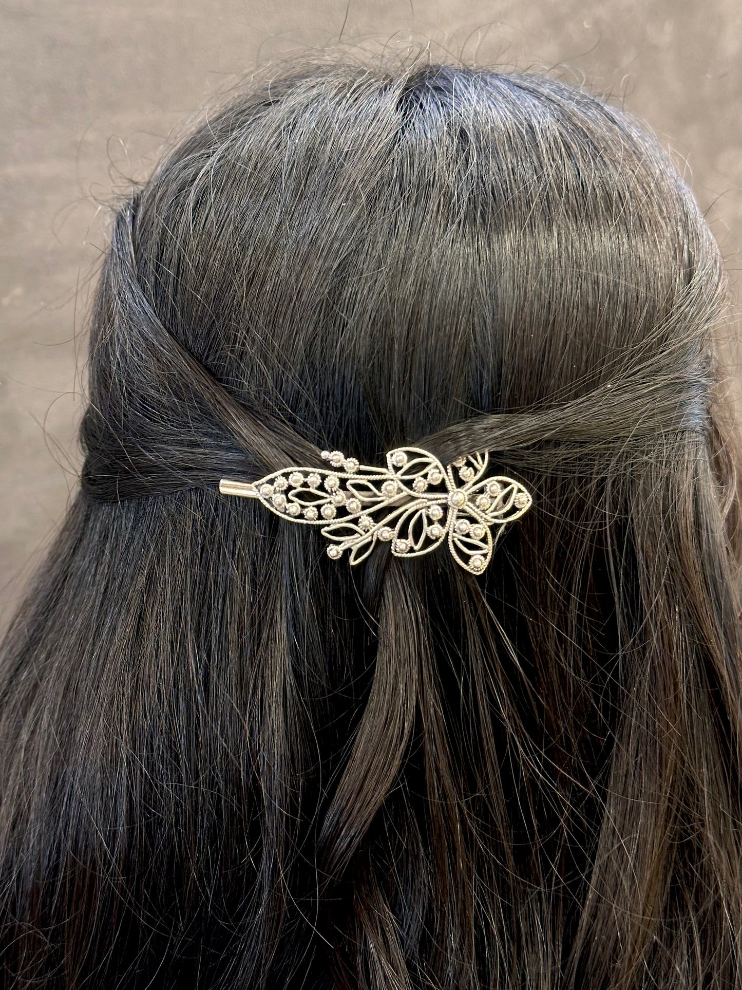 Gold leaf hairpin in a person's hair against a neutral background