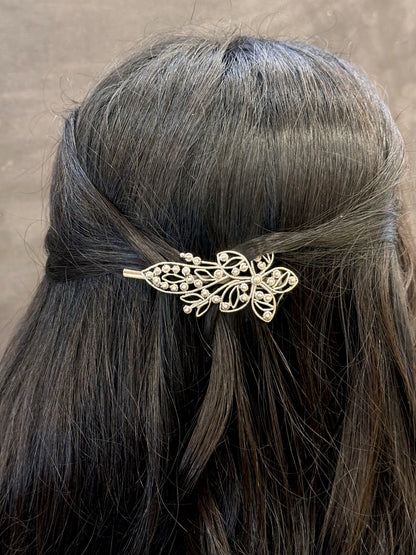 Gold leaf hairpin in a person's hair against a neutral background