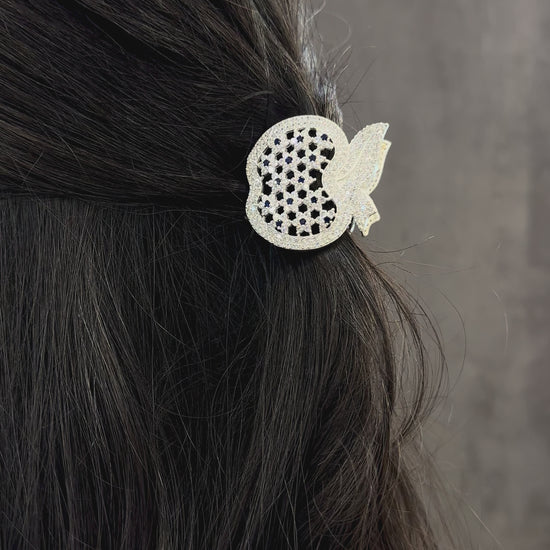 Decorative hair clip with black and clear gemstones on dark hair against a neutral background