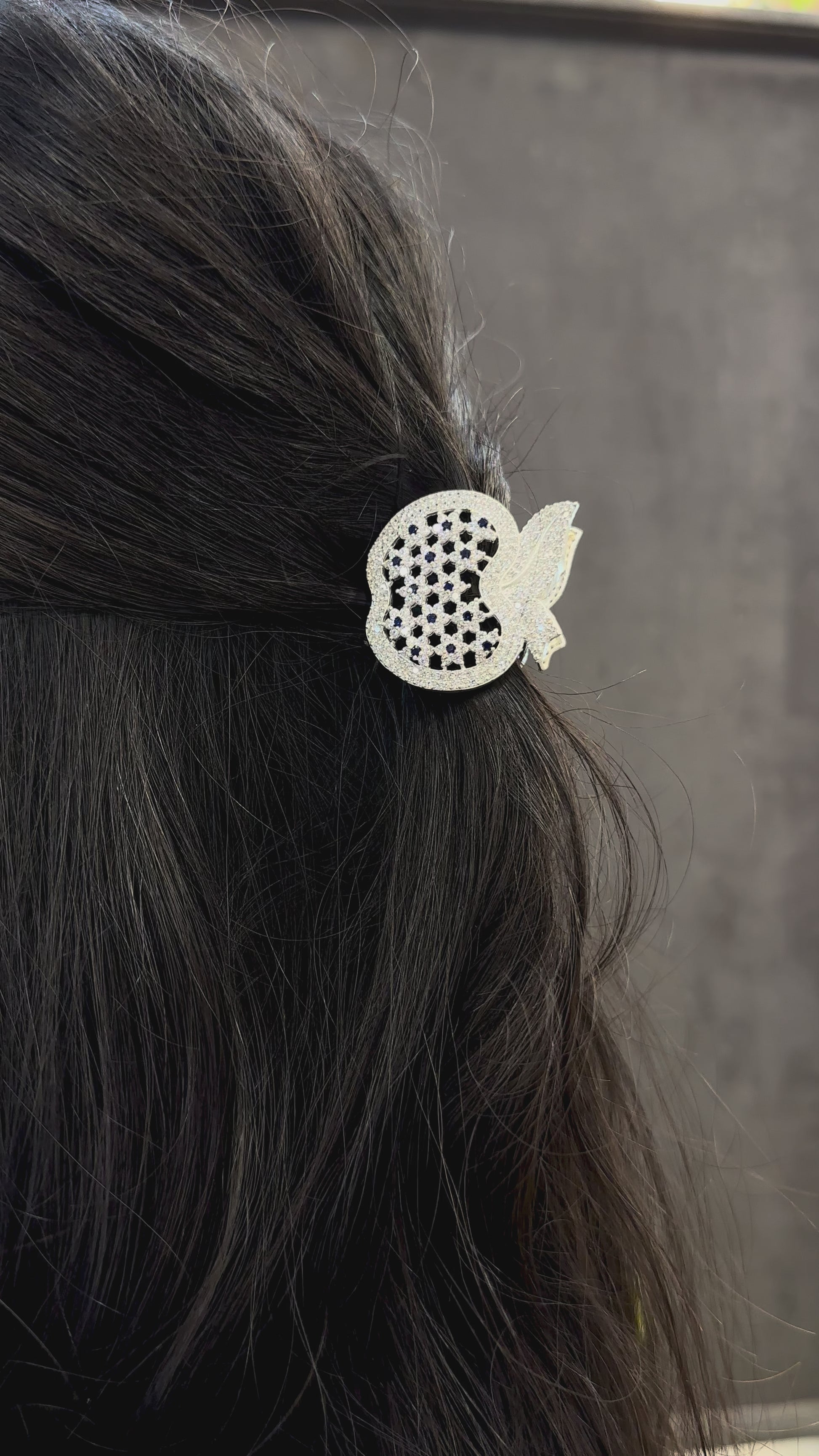 Decorative hair clip with black and clear gemstones on dark hair against a neutral background