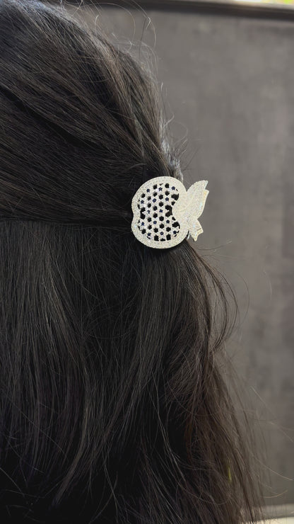 Decorative hair clip with black and clear gemstones on dark hair against a neutral background