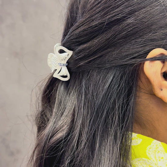 Silver hair clip with blue stones on black hair against a dark background