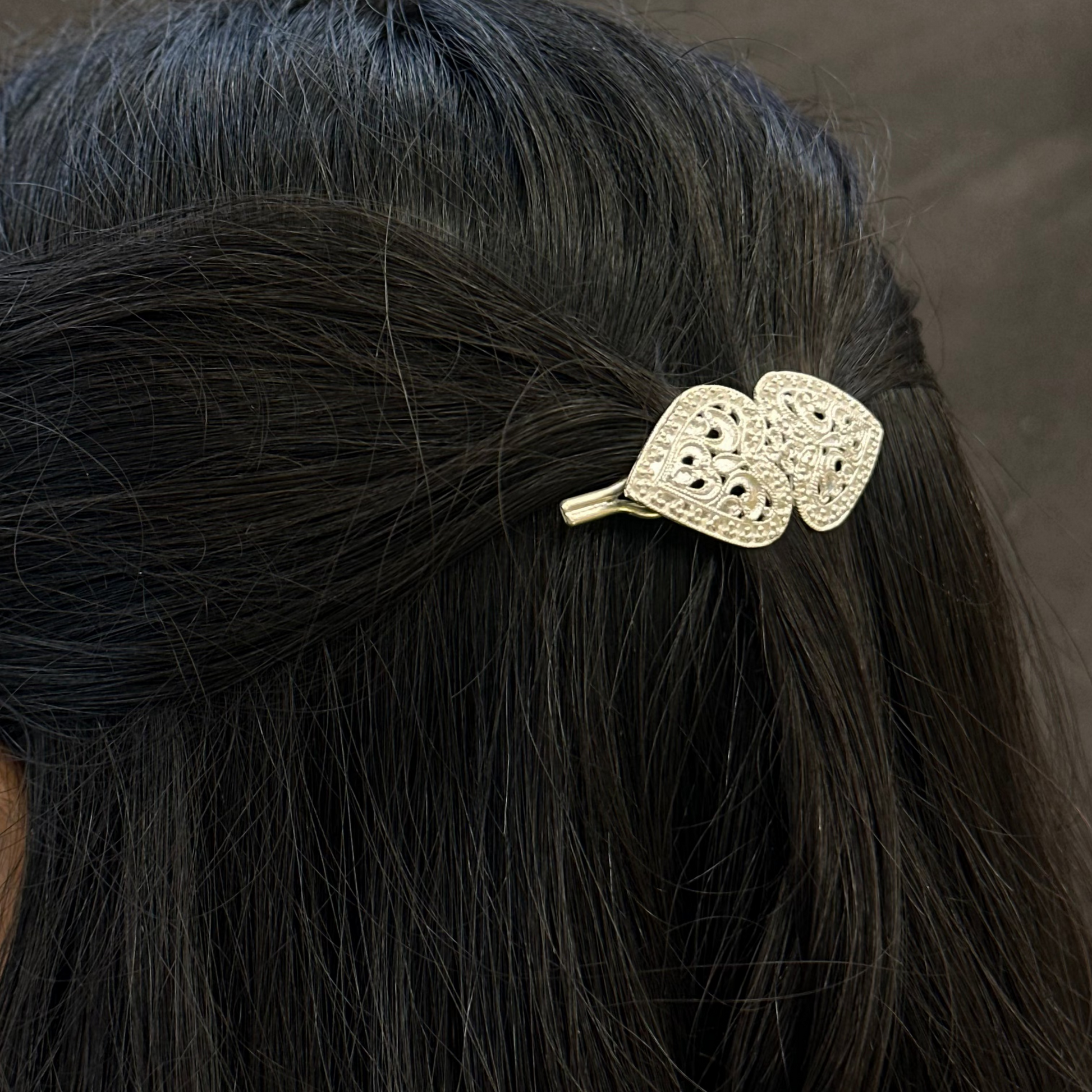 Hair clip with decorative design in a person's hair against a dark background