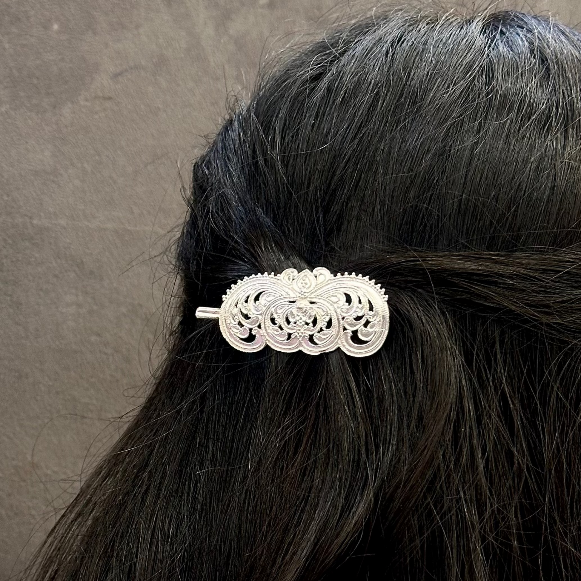 Silver hair clip on black hair against a gray background