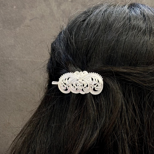 Silver hair clip on black hair against a gray background