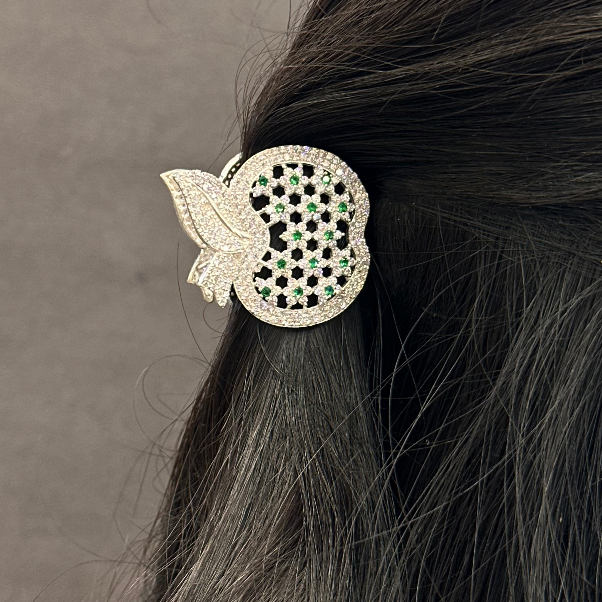 Decorative hair clip with black and clear gemstones on dark hair against a neutral background
