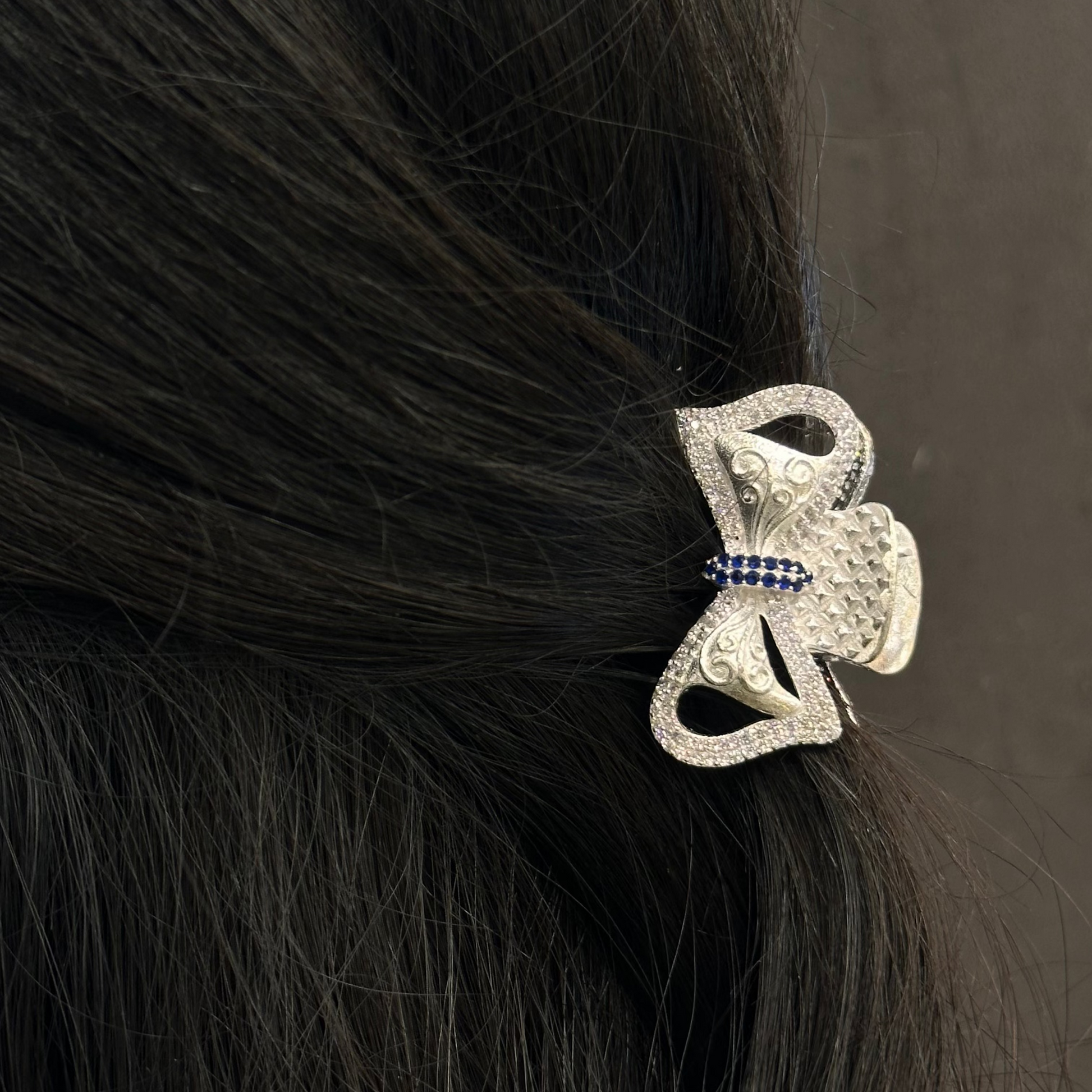 Silver hair clip with blue stones on black hair against a dark background