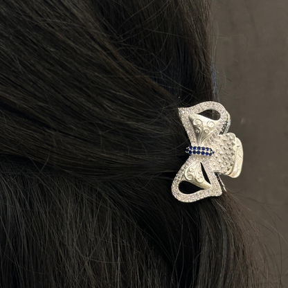 Silver hair clip with blue stones on black hair against a dark background